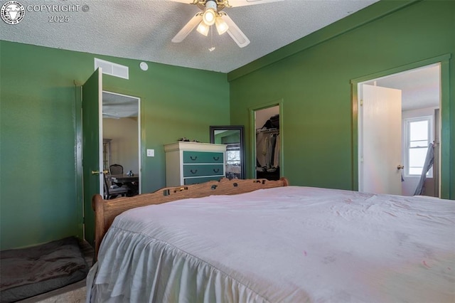 bedroom featuring ceiling fan, a closet, a textured ceiling, and a walk in closet