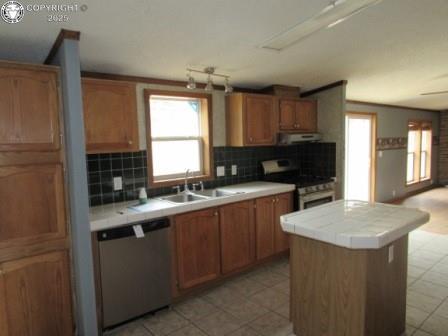 kitchen featuring a sink, stainless steel appliances, tile counters, under cabinet range hood, and decorative backsplash