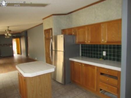 kitchen with freestanding refrigerator, brown cabinetry, open floor plan, backsplash, and light countertops