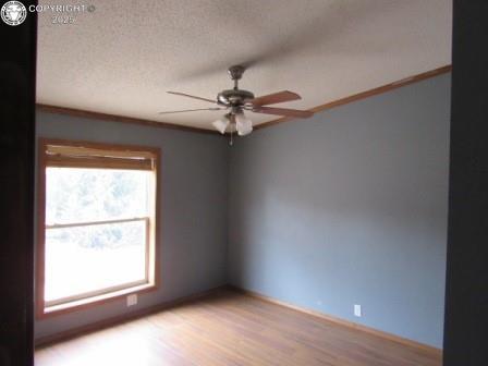 unfurnished room with a textured ceiling, light wood-type flooring, crown molding, a ceiling fan, and baseboards