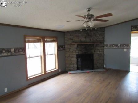 unfurnished living room with ceiling fan, baseboards, a large fireplace, and wood finished floors