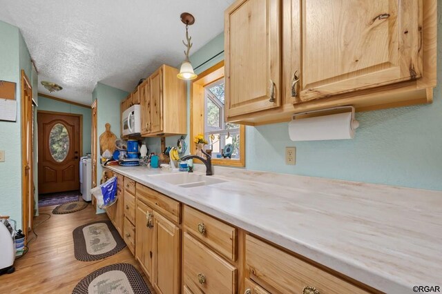 kitchen with pendant lighting, light brown cabinetry, light hardwood / wood-style floors, and a textured ceiling