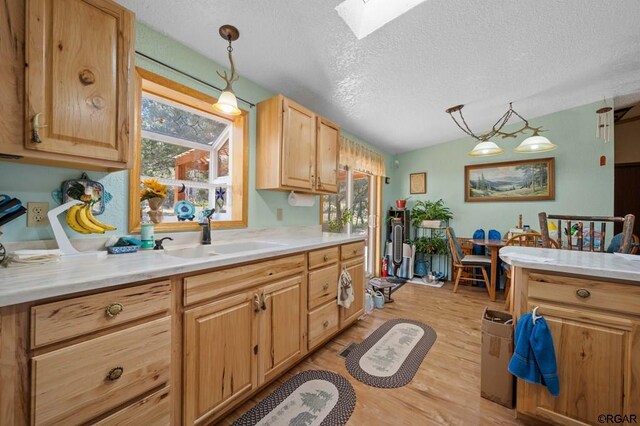 kitchen with sink, hanging light fixtures, light wood-type flooring, light brown cabinets, and a textured ceiling