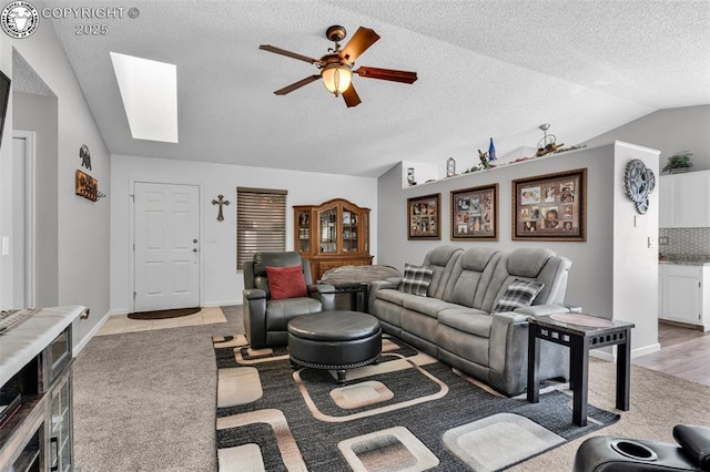 living room featuring baseboards, vaulted ceiling with skylight, a textured ceiling, and a ceiling fan