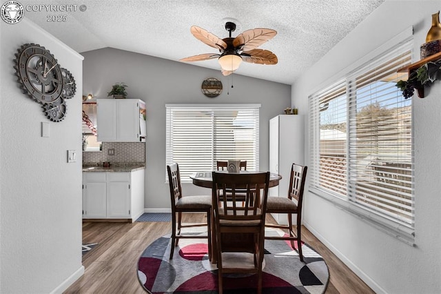 dining area featuring vaulted ceiling, light wood finished floors, and a textured ceiling