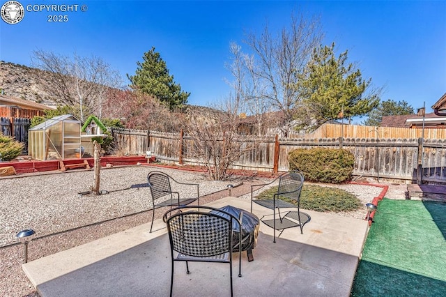 view of patio with an outdoor structure, a greenhouse, and a fenced backyard