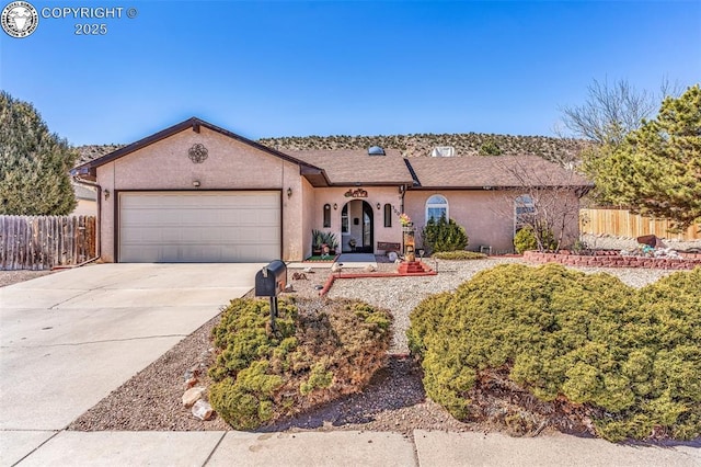 view of front facade with stucco siding, an attached garage, driveway, and fence