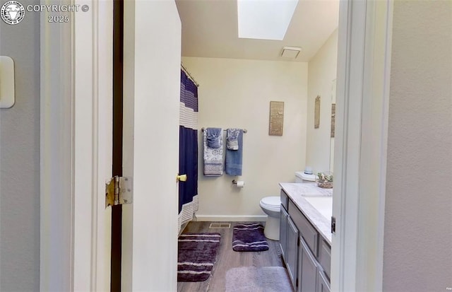 bathroom featuring vanity, wood finished floors, baseboards, a skylight, and toilet