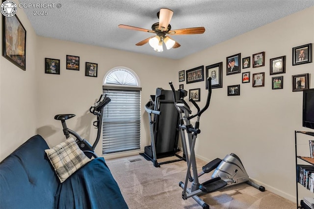 workout room featuring ceiling fan, light colored carpet, baseboards, and a textured ceiling