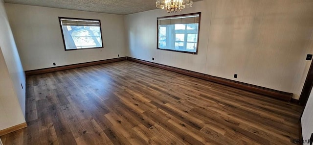 unfurnished room with a chandelier, dark hardwood / wood-style floors, and a textured ceiling