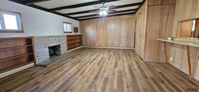 unfurnished living room featuring a stone fireplace, wooden walls, a baseboard heating unit, beam ceiling, and light hardwood / wood-style flooring