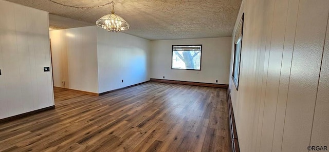 spare room with dark wood-type flooring, wooden walls, a notable chandelier, and a textured ceiling