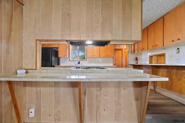 kitchen featuring hardwood / wood-style flooring, black refrigerator, white gas stovetop, decorative backsplash, and a baseboard radiator