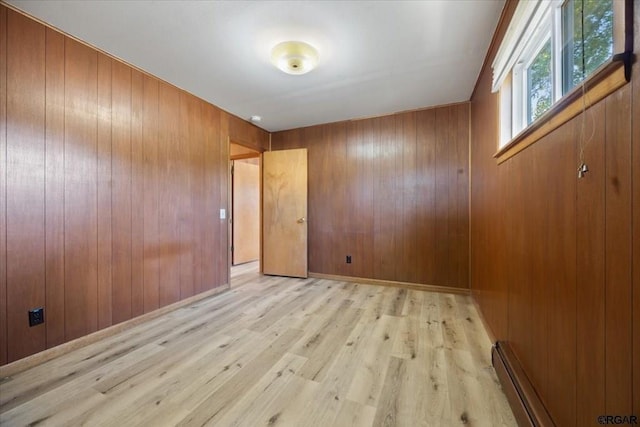 spare room featuring light hardwood / wood-style flooring, a baseboard heating unit, and wooden walls