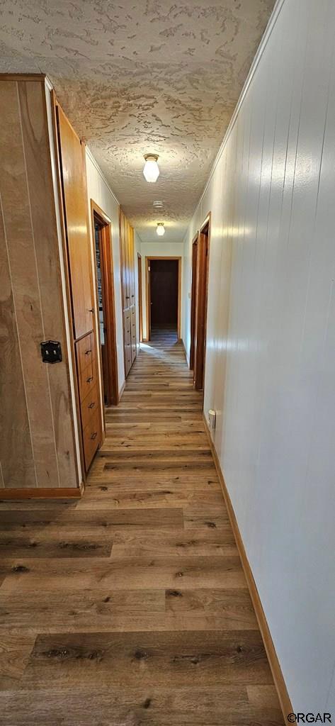 corridor featuring hardwood / wood-style flooring, ornamental molding, wooden walls, and a textured ceiling