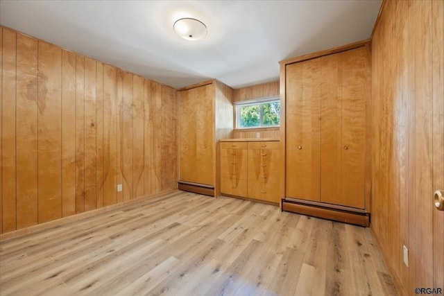 unfurnished room featuring a baseboard radiator, light hardwood / wood-style floors, and wood walls