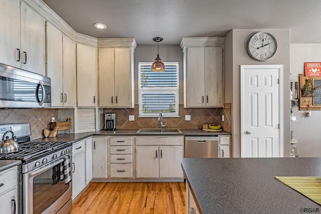 kitchen with sink, tasteful backsplash, decorative light fixtures, light wood-type flooring, and appliances with stainless steel finishes