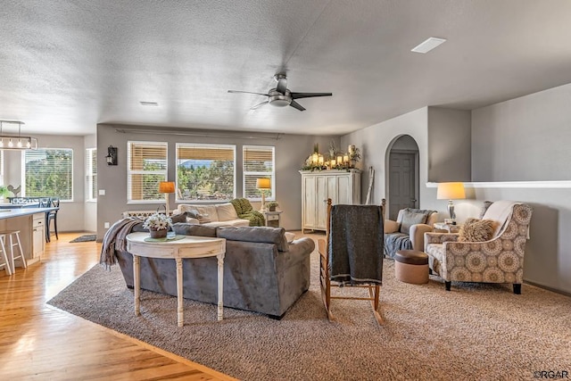 living room featuring ceiling fan with notable chandelier, a textured ceiling, and light wood-type flooring