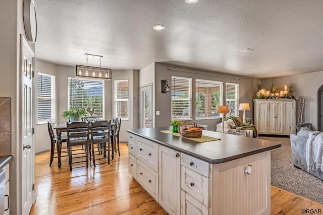 kitchen with white cabinetry, decorative light fixtures, a center island, white dishwasher, and light hardwood / wood-style floors