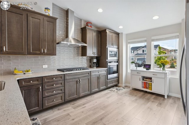 16840 New Autumn Dr, Monument, CO 80132 - kitchen with wall chimney range hood, appliances with stainless steel finishes, decorative backsplash, dark brown cabinets, and light wood-type flooring