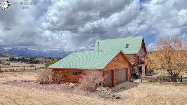 view of side of home with a mountain view, fence, dirt driveway, metal roof, and a garage