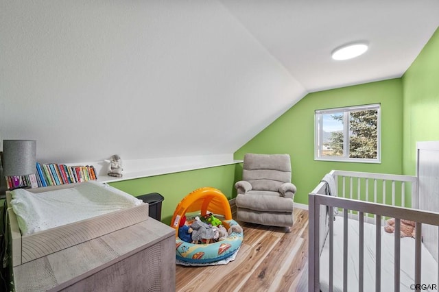 bedroom featuring hardwood / wood-style flooring, vaulted ceiling, and a crib