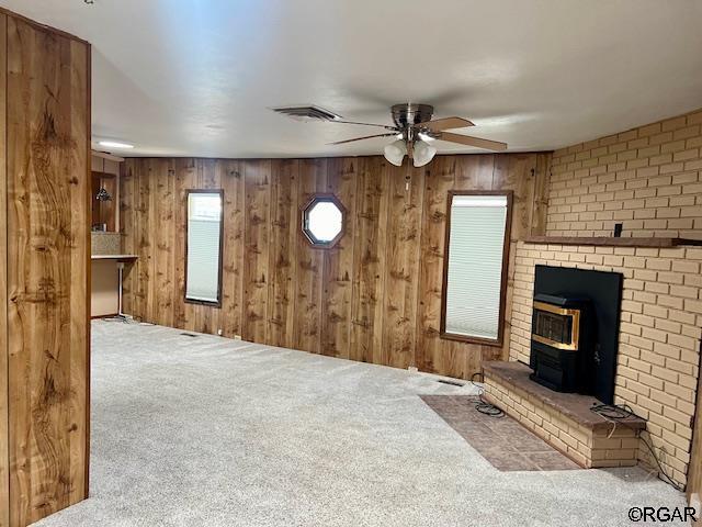 unfurnished living room featuring ceiling fan, wooden walls, light colored carpet, and a wood stove