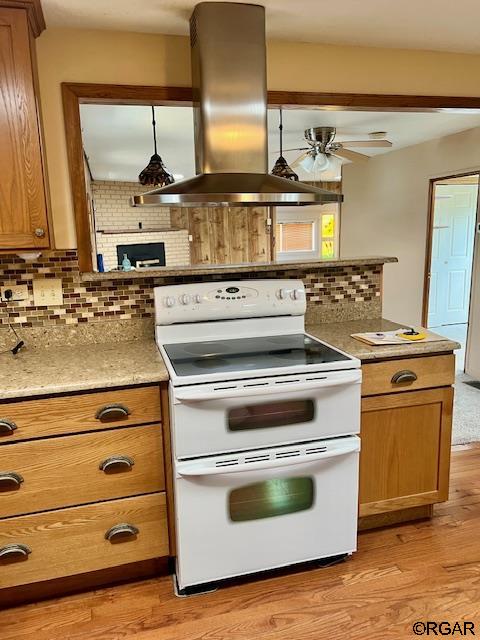 kitchen featuring island range hood, double oven range, light wood-type flooring, and backsplash