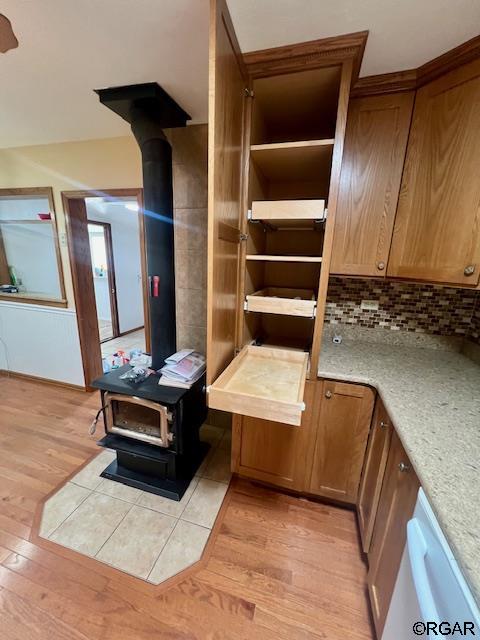 interior details with tasteful backsplash, dishwasher, a wood stove, light hardwood / wood-style floors, and light stone countertops