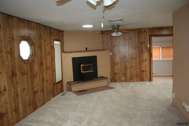 living room featuring a wood stove, light colored carpet, ceiling fan, and wood walls