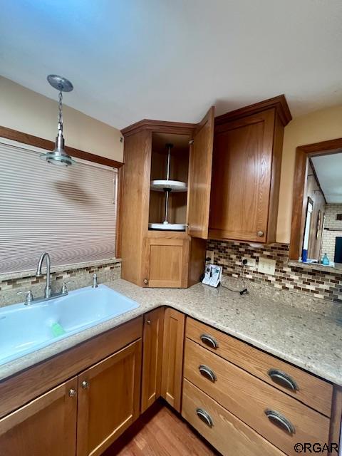 kitchen featuring sink, light stone counters, light hardwood / wood-style floors, decorative backsplash, and decorative light fixtures