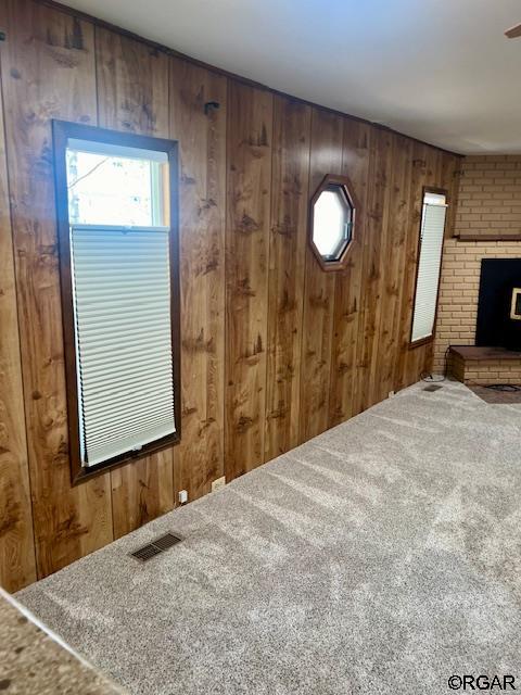 unfurnished living room with carpet, wooden walls, and a brick fireplace