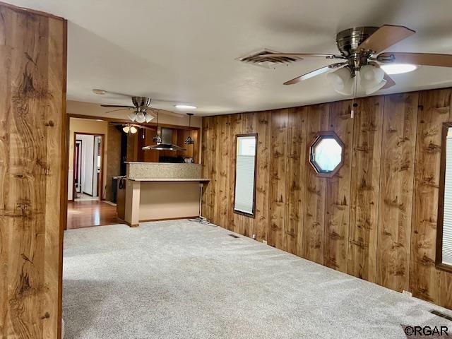 unfurnished living room with wooden walls, light carpet, and ceiling fan