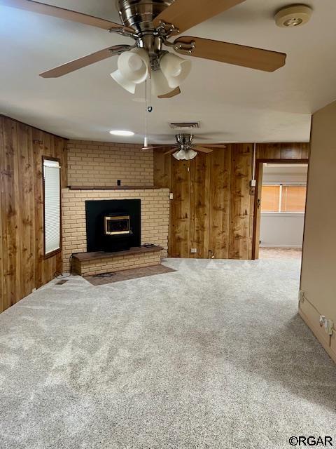 unfurnished living room featuring ceiling fan, carpet floors, a fireplace, and wood walls