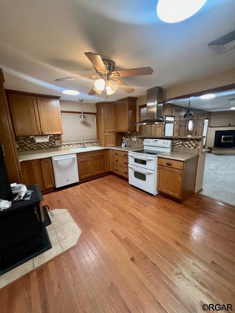 kitchen with wall chimney exhaust hood, decorative light fixtures, light wood-type flooring, white appliances, and decorative backsplash