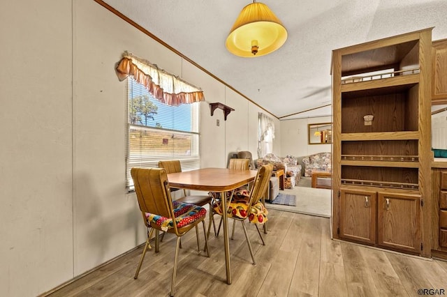 dining space with crown molding, lofted ceiling, and light wood-type flooring