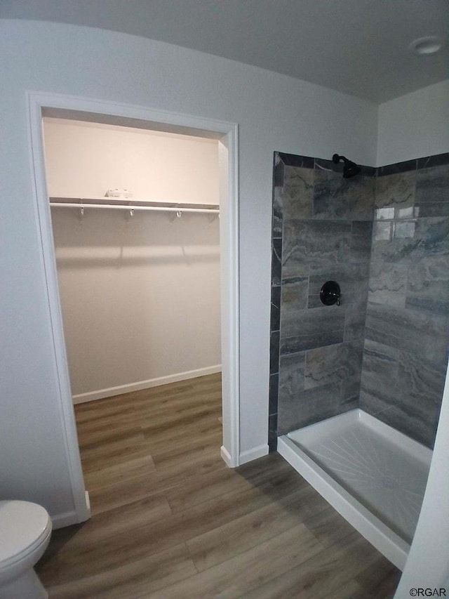 bathroom with hardwood / wood-style flooring, tiled shower, and toilet