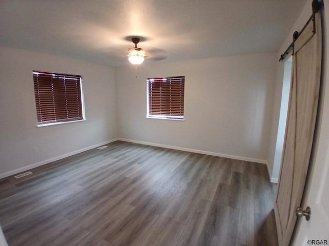 unfurnished room with dark wood-type flooring, a barn door, and ceiling fan