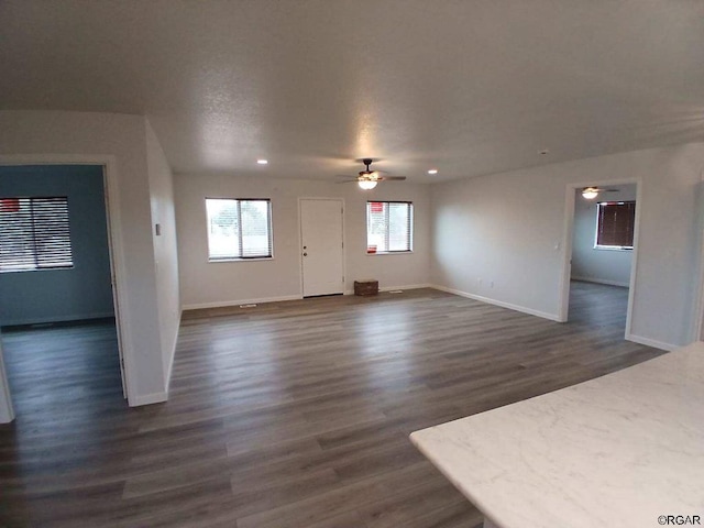 unfurnished living room featuring dark wood-type flooring and ceiling fan