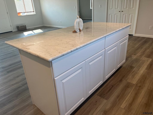 kitchen featuring dark hardwood / wood-style flooring, light stone countertops, a center island, and white cabinets