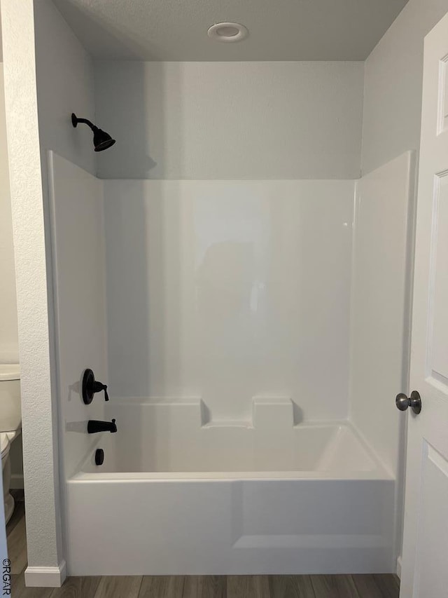 bathroom featuring wood-type flooring, bathtub / shower combination, and toilet