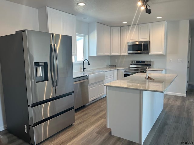 kitchen with a kitchen island, white cabinets, stainless steel appliances, light stone countertops, and dark wood-type flooring