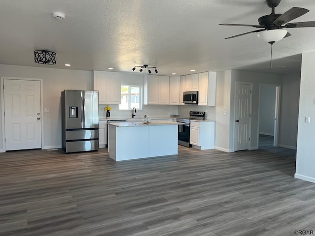 kitchen with appliances with stainless steel finishes, white cabinetry, dark hardwood / wood-style floors, a center island, and a textured ceiling