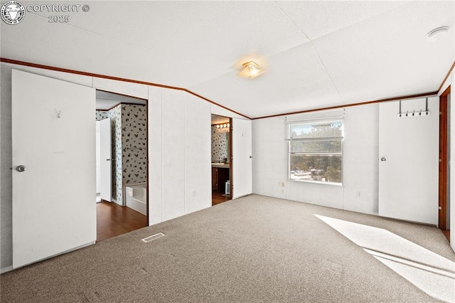 unfurnished bedroom featuring dark carpet, ensuite bath, and vaulted ceiling