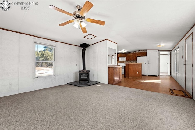 unfurnished living room with vaulted ceiling, light colored carpet, ceiling fan, and a wood stove