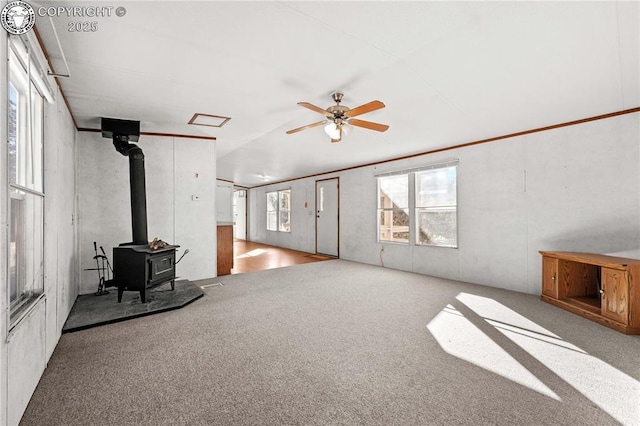 unfurnished living room featuring light carpet, plenty of natural light, ceiling fan, and a wood stove