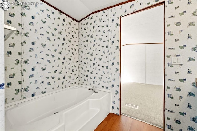 bathroom featuring wood-type flooring, lofted ceiling, ornamental molding, and a washtub