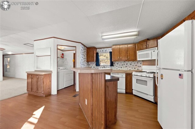 kitchen with white appliances, a center island, a textured ceiling, separate washer and dryer, and light wood-type flooring