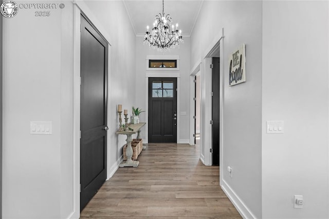 entrance foyer featuring ornamental molding, light wood finished floors, a chandelier, and baseboards