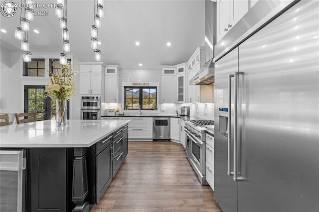 kitchen featuring premium appliances, wine cooler, white cabinetry, a center island, and glass insert cabinets